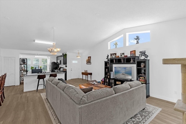 living room with sink, lofted ceiling, light hardwood / wood-style flooring, and an inviting chandelier