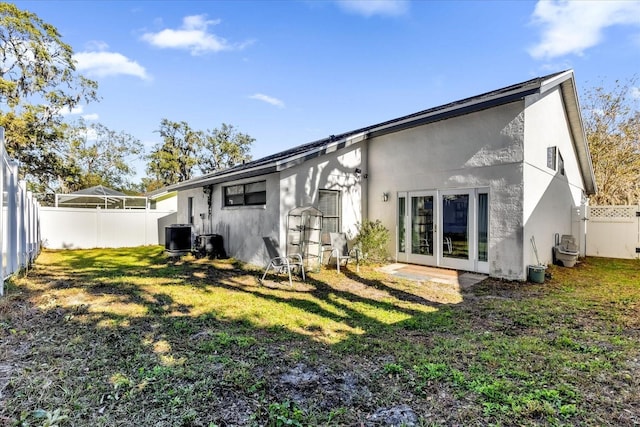 back of property featuring french doors, central air condition unit, and a lawn