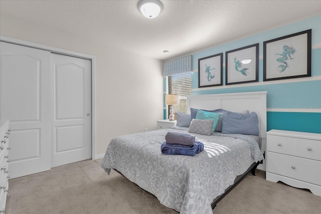 bedroom with a textured ceiling, light colored carpet, and a closet