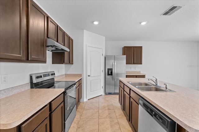 kitchen with light tile patterned flooring, stainless steel appliances, a kitchen island with sink, and sink