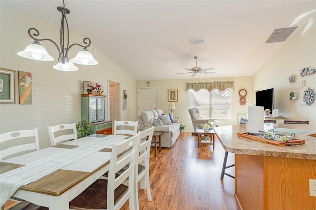 dining room with light hardwood / wood-style floors, ceiling fan with notable chandelier, and vaulted ceiling