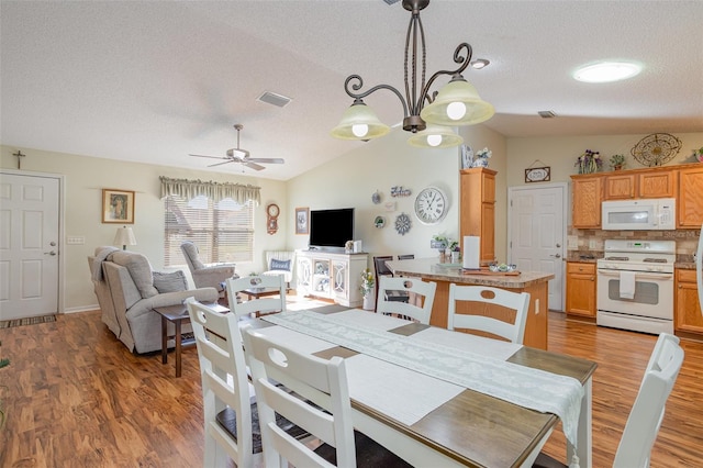 dining room with wood-type flooring, ceiling fan with notable chandelier, a textured ceiling, and lofted ceiling