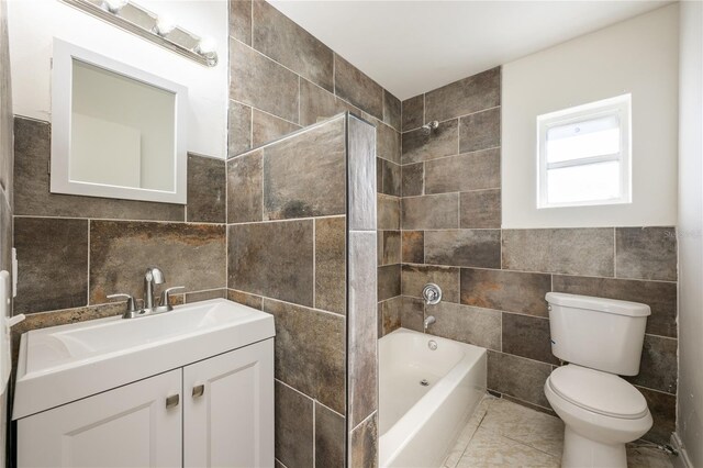 full bathroom with tile patterned floors, vanity, tile walls, washtub / shower combination, and toilet