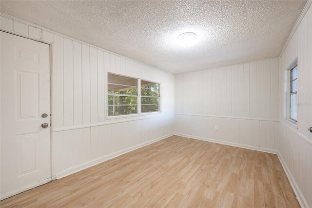 unfurnished room featuring wooden walls, a textured ceiling, and light wood-type flooring