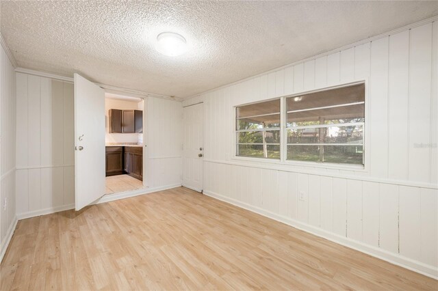 spare room featuring a textured ceiling, light wood-type flooring, and wood walls