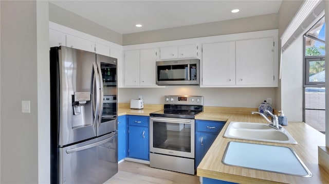 kitchen with white cabinets, blue cabinets, sink, appliances with stainless steel finishes, and light hardwood / wood-style floors