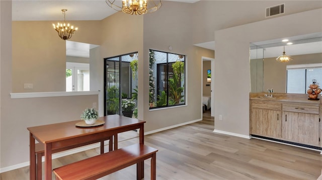 dining area with a notable chandelier, light wood-type flooring, sink, and lofted ceiling