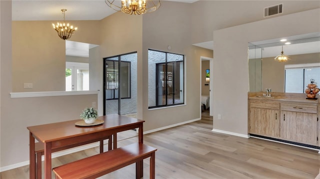 dining area featuring sink, light hardwood / wood-style floors, vaulted ceiling, and an inviting chandelier