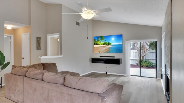 living room with ceiling fan, high vaulted ceiling, a textured ceiling, and light wood-type flooring