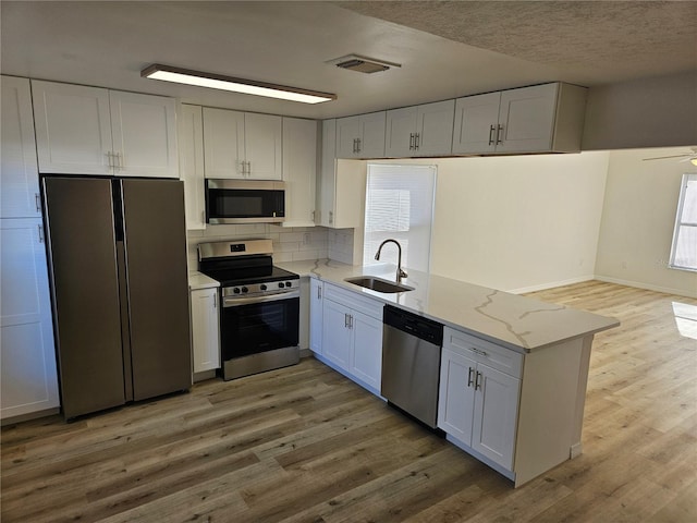 kitchen with light stone countertops, white cabinetry, sink, stainless steel appliances, and hardwood / wood-style flooring