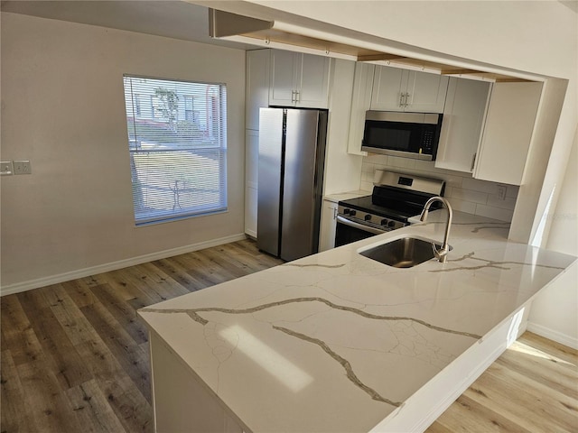 kitchen featuring sink, stainless steel appliances, light stone counters, light hardwood / wood-style flooring, and kitchen peninsula