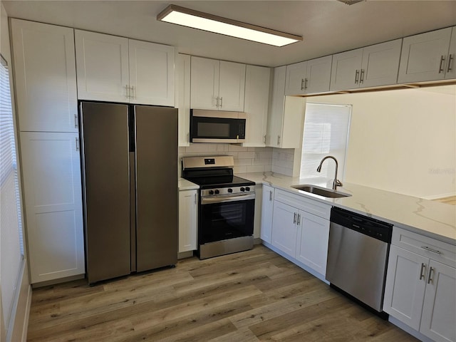 kitchen featuring sink, appliances with stainless steel finishes, light hardwood / wood-style floors, light stone counters, and white cabinetry