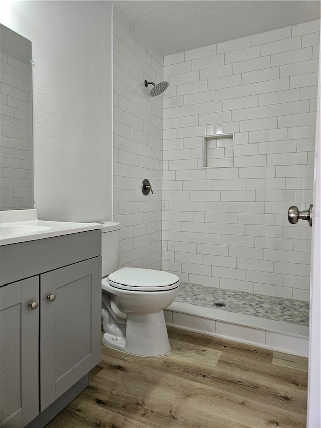 bathroom with wood-type flooring, vanity, a tile shower, and toilet