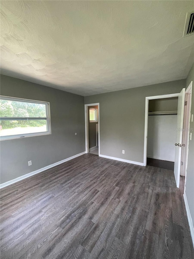 unfurnished bedroom with a textured ceiling, dark hardwood / wood-style flooring, and a closet