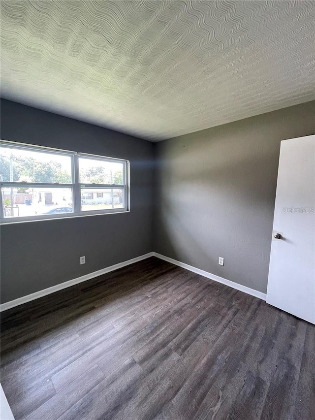 unfurnished room featuring dark wood-type flooring and a textured ceiling