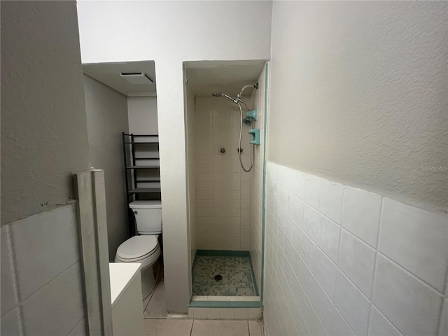 bathroom with tiled shower, tile patterned floors, toilet, and tile walls