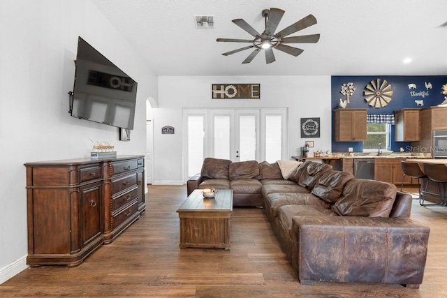 living room with baseboards, visible vents, a ceiling fan, arched walkways, and dark wood-type flooring