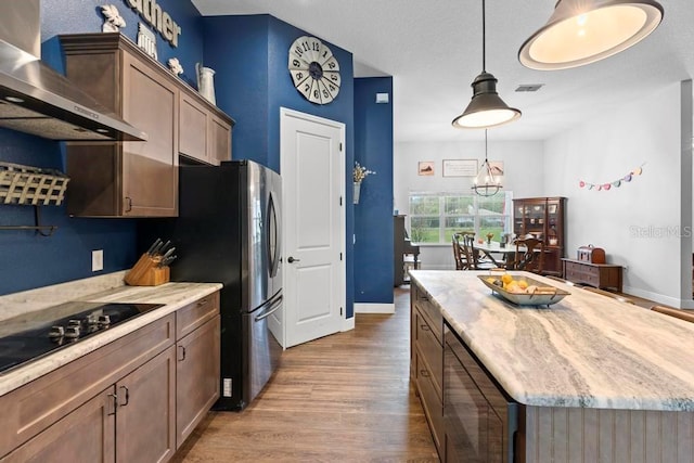 kitchen featuring pendant lighting, light countertops, a kitchen island, wall chimney range hood, and wood finished floors