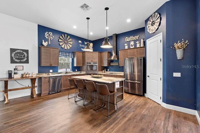 kitchen with visible vents, wall chimney exhaust hood, a kitchen island, appliances with stainless steel finishes, and decorative light fixtures