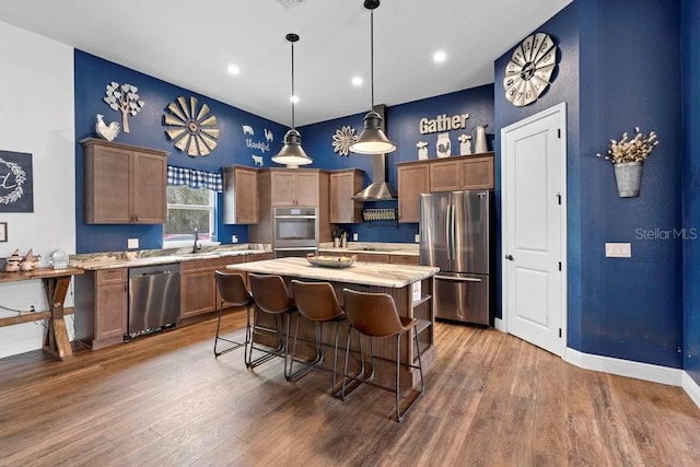 kitchen featuring wall chimney exhaust hood, a kitchen island, hanging light fixtures, stainless steel appliances, and a sink