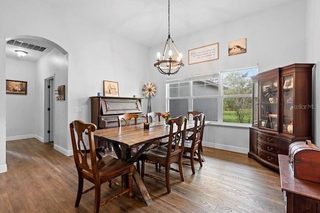 dining area featuring baseboards, visible vents, arched walkways, and wood finished floors