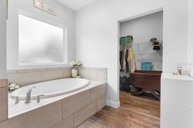 bathroom with a spacious closet, wood finished floors, and a garden tub