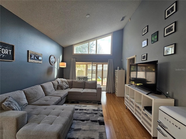 living room with high vaulted ceiling, a textured ceiling, and light wood-type flooring