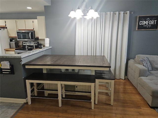 kitchen with kitchen peninsula, appliances with stainless steel finishes, a notable chandelier, dark hardwood / wood-style flooring, and white cabinetry