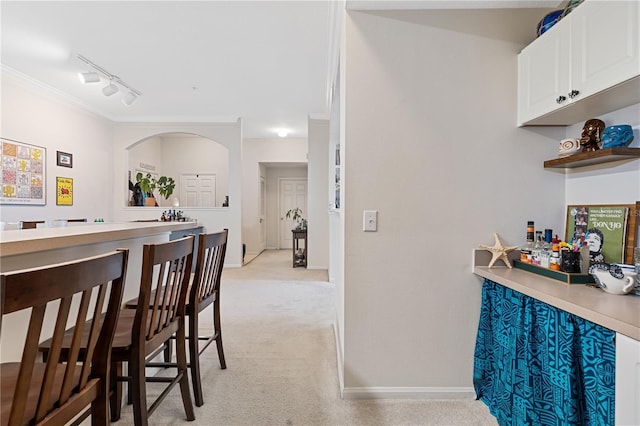 interior space with white cabinetry, crown molding, light colored carpet, and rail lighting