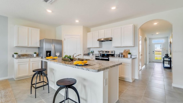 kitchen with a kitchen island with sink, sink, light tile patterned floors, appliances with stainless steel finishes, and white cabinetry