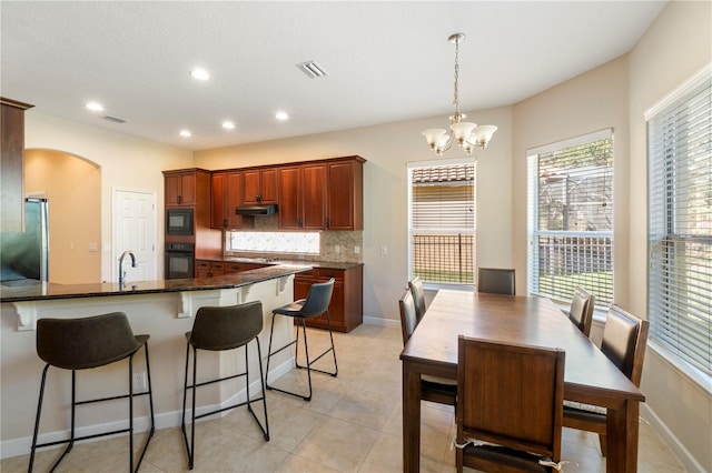 kitchen featuring dark stone countertops, a chandelier, pendant lighting, decorative backsplash, and black appliances