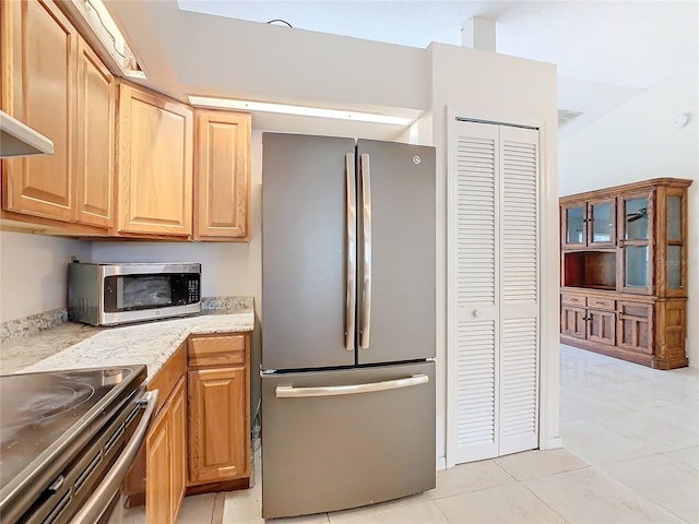 kitchen with light stone counters, light tile patterned floors, exhaust hood, and appliances with stainless steel finishes