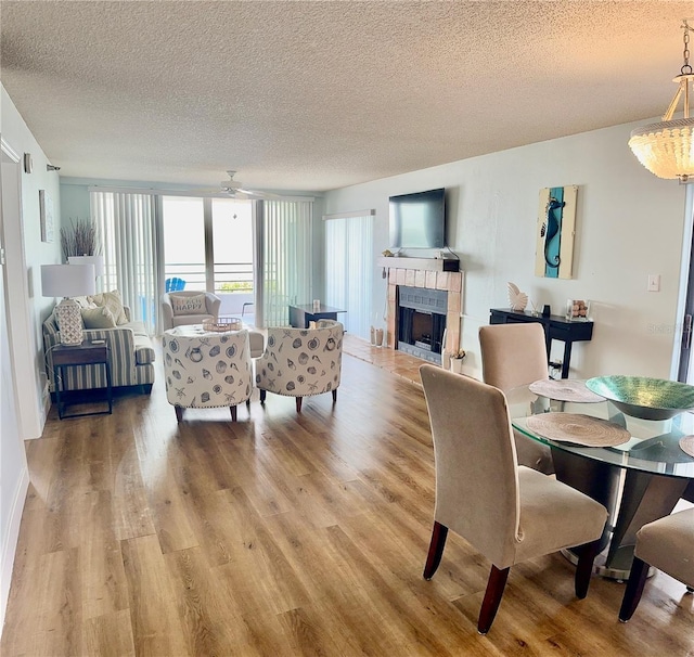 dining room featuring a textured ceiling, ceiling fan, light wood-type flooring, and a fireplace