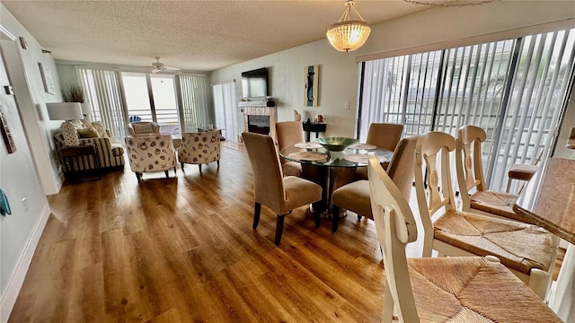 dining space featuring a tile fireplace, ceiling fan with notable chandelier, wood-type flooring, and a textured ceiling