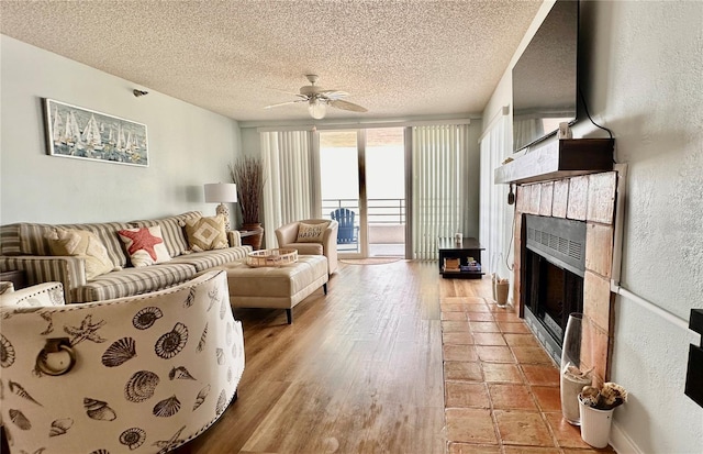 living room with ceiling fan, a fireplace, light hardwood / wood-style floors, and a textured ceiling