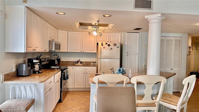 kitchen with appliances with stainless steel finishes, decorative columns, a tray ceiling, white cabinets, and light tile patterned flooring