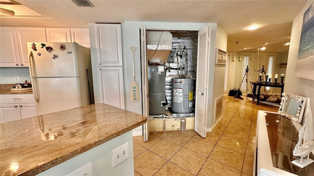 kitchen with light stone countertops, electric water heater, light tile patterned floors, white refrigerator, and white cabinets