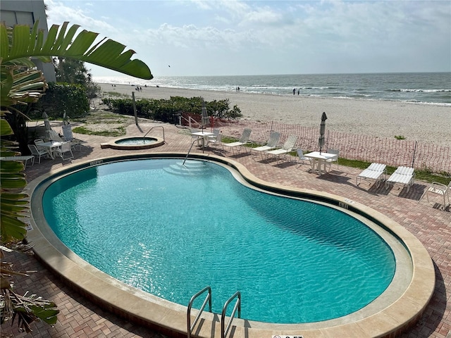 view of swimming pool featuring a water view, a beach view, and a patio