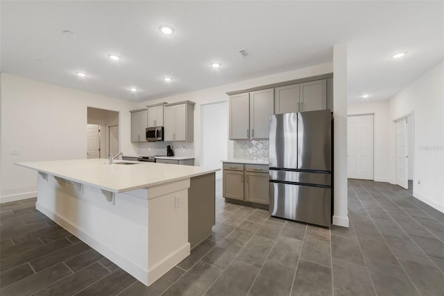 kitchen with backsplash, gray cabinetry, stainless steel appliances, sink, and an island with sink