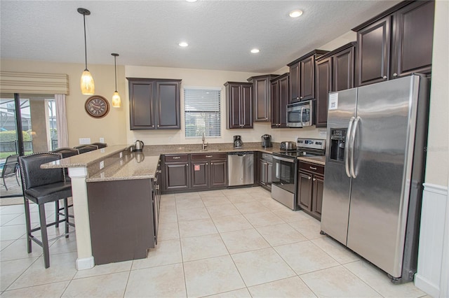 kitchen featuring light stone countertops, stainless steel appliances, kitchen peninsula, pendant lighting, and a breakfast bar area