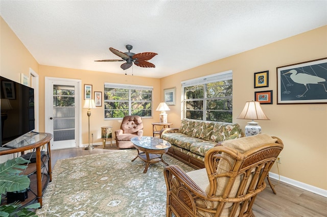 living room with ceiling fan, light wood-type flooring, and a textured ceiling