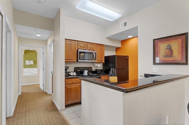 kitchen featuring dark stone counters, kitchen peninsula, light tile patterned floors, and black appliances