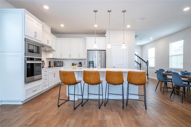 kitchen featuring a kitchen island with sink, decorative light fixtures, light hardwood / wood-style floors, white cabinetry, and stainless steel appliances