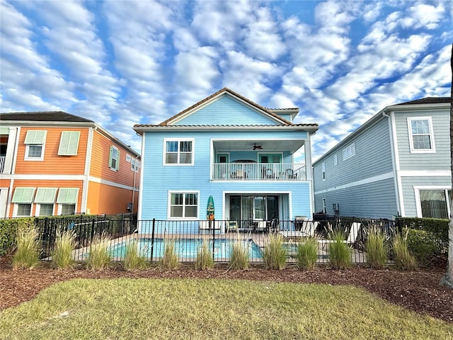 back of property featuring ceiling fan, a lawn, a fenced in pool, a balcony, and a patio