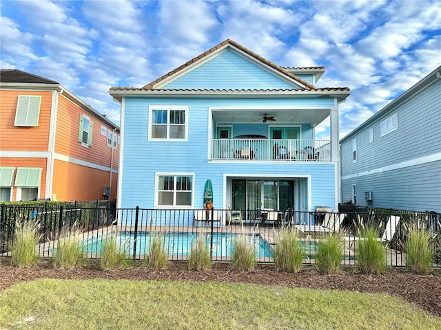 rear view of house with ceiling fan, a yard, a balcony, and a fenced in pool