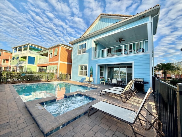 back of house with a balcony, a swimming pool with hot tub, ceiling fan, and a patio