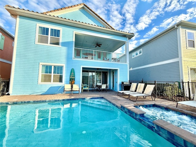 rear view of house with ceiling fan, a pool with hot tub, a balcony, and a patio