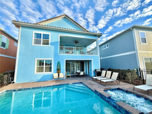 rear view of house with ceiling fan, a patio area, a pool with hot tub, and a balcony