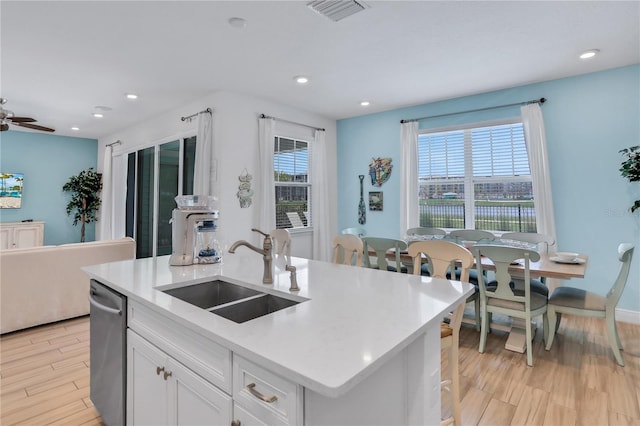 kitchen with a center island with sink, ceiling fan, stainless steel dishwasher, white cabinets, and sink