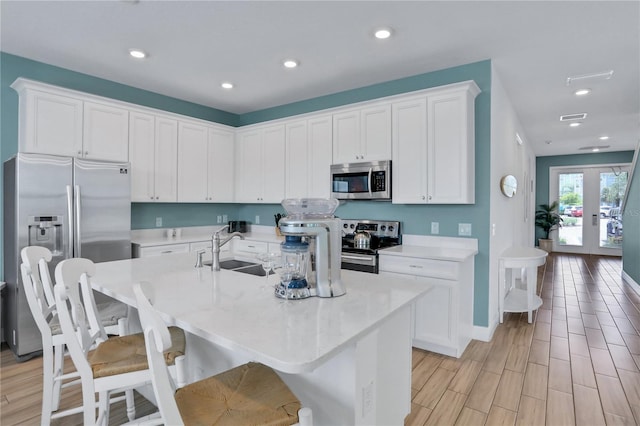 kitchen with appliances with stainless steel finishes, white cabinetry, french doors, an island with sink, and sink